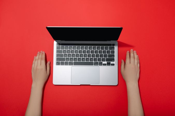 Top view of person’s hands resting next to laptop keyboard on red table