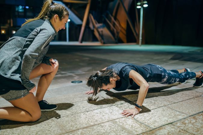 Woman doing push ups with personal trainer in the city at night