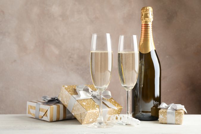 Gift boxes, champagne glasses and bottle against brown background, space for text