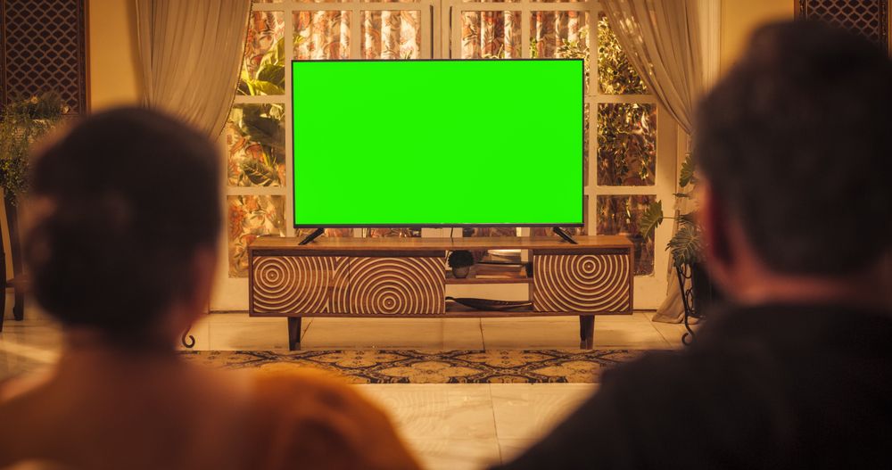 Back View of Older Indian Couple Watching Green Mock-up Screen Chroma Key TV while Sitting on a Couch in the Living Room.