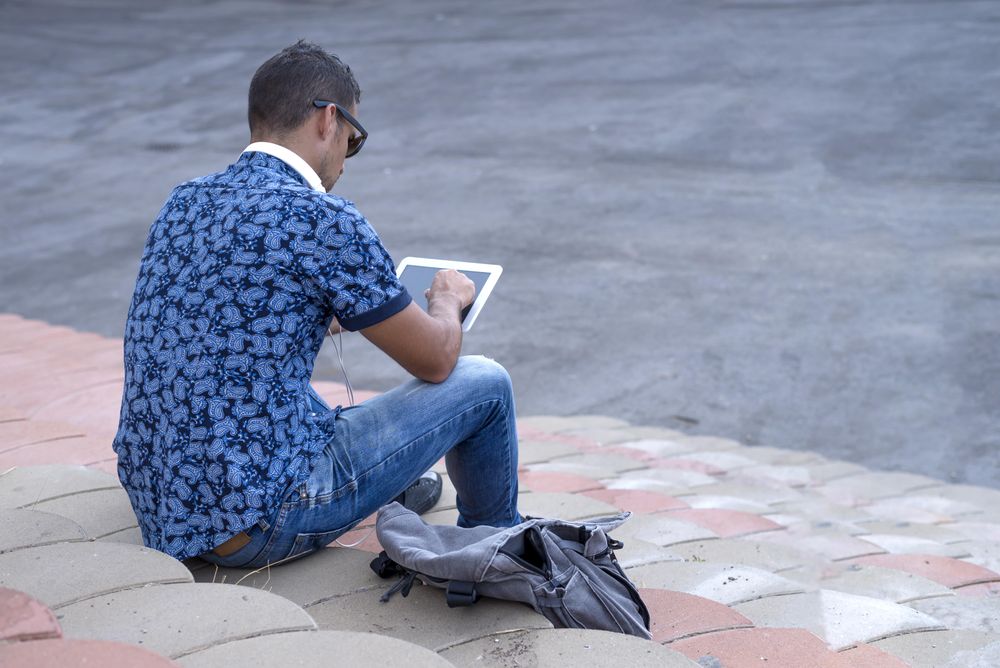 Rear of male sitting on stairs on sunny day and using tablet