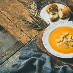 Pumpkin soup with croutons, and bread on wooden table, square crop