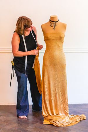 A fashion designer is pinning cut out pieces of fabric to mannequin.
