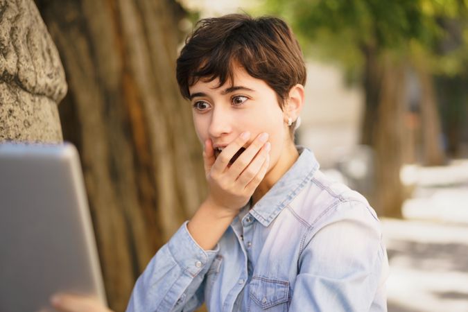 A surprised young woman is reacting with curiosity to her laptop screen while outdoors