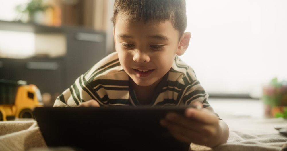 Portrait of an Asian Male Kid Using Digital Tablet, Smiling in his Room.