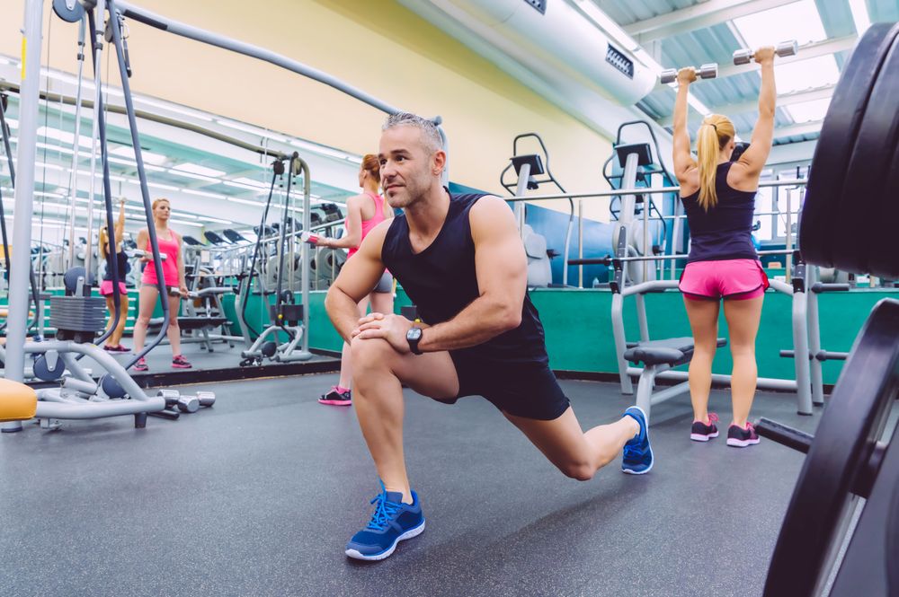 Male stretching legs in busy gym