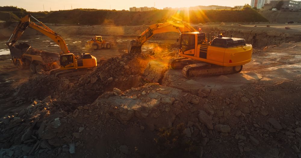 Aerial Drone Shot Of Construction Site On Sunny Day: Industrial Excavators Digging Rocks To Lay Foundation For A New Apartment Complex. People Using Heavy Machinery To Complete A Real Estate Project.
