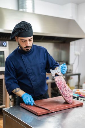 Cook with large piece of raw meat in kitchen