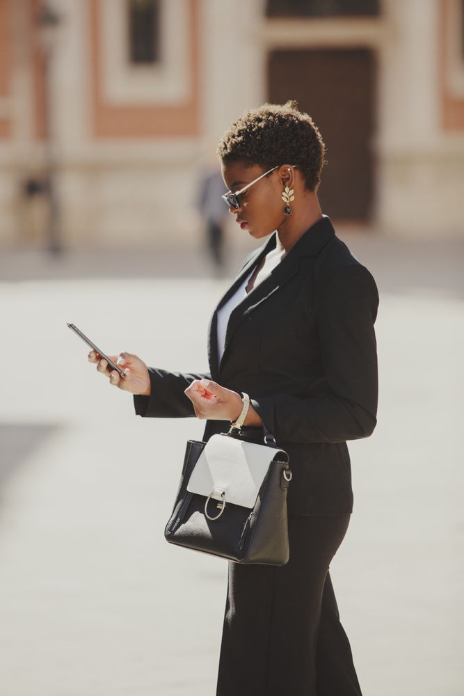 Stylish Black woman with handbag and smartphone on street
