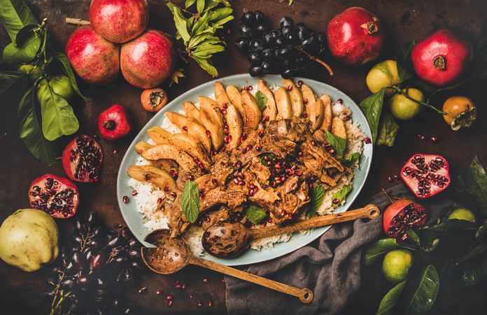 Plate of lamp chops over rice, and quince on table with grapes and pomegranate