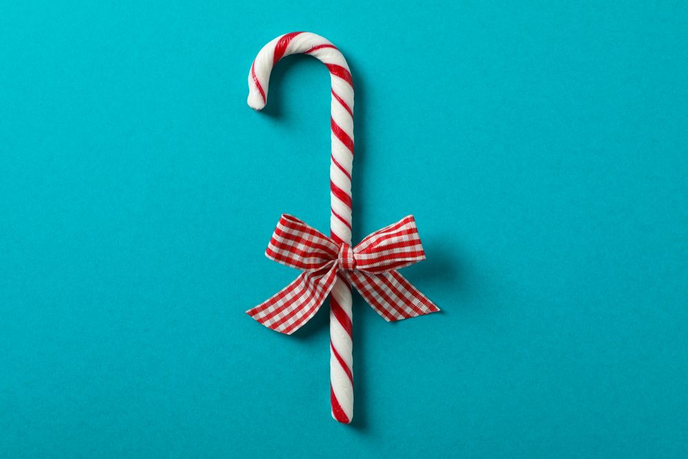 Sweet candy cane with bow on turquoise background, space for text