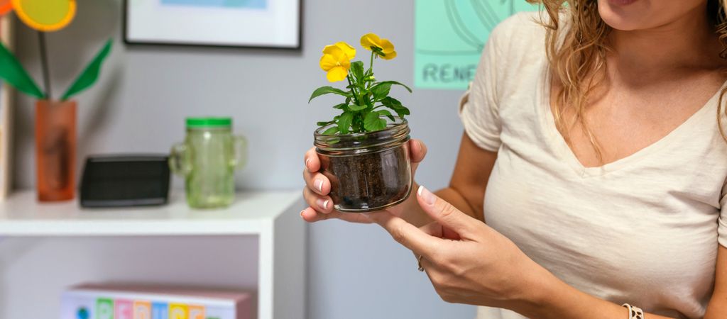 Woman holding a pansy plant inside of glass pot in ecology classroom