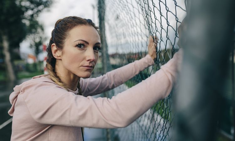 Sporty woman resting on sports court fence
