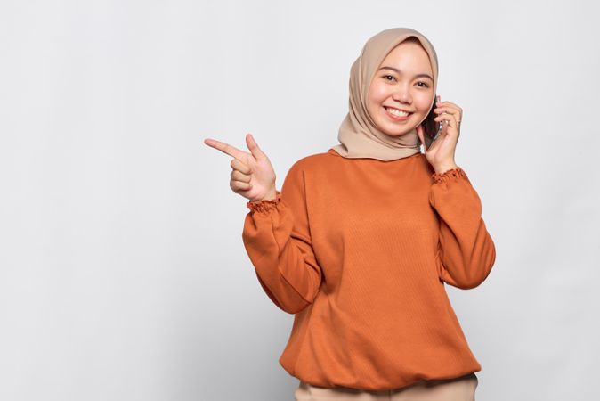 Smiling Muslim woman talking on cell phone and pointing