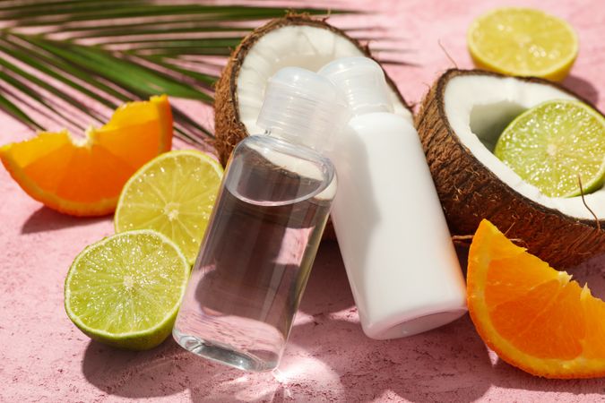 Coconut, fruits and cosmetics on pink background, close up