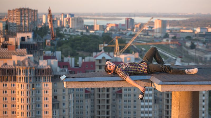 Male lying back with bottle of wine in hand on roof