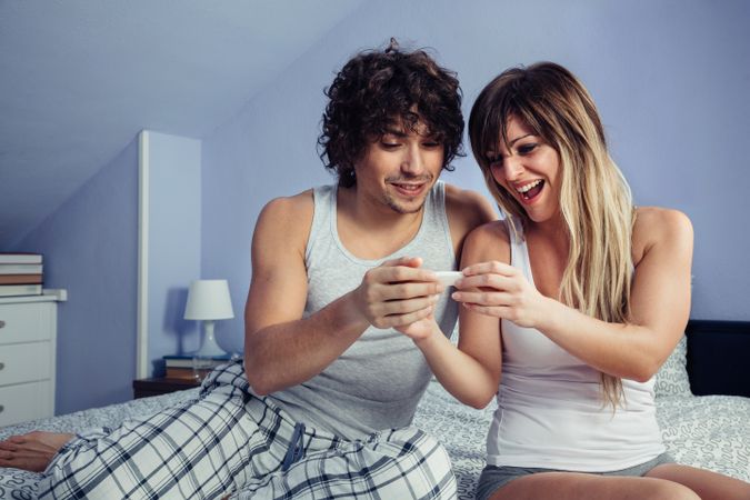 Smiling couple looking pregnancy test in bedroom