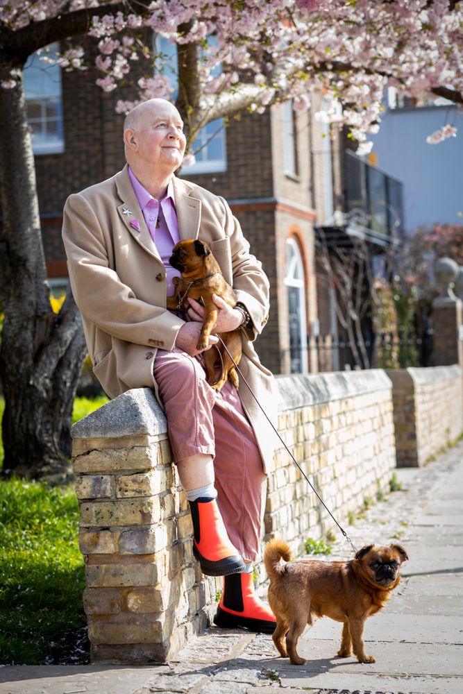 Mature man sitting on wall with two dogs and spring blossoms in the background