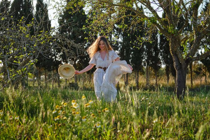 Cheerful woman in stylish sundress walking on grassy meadow