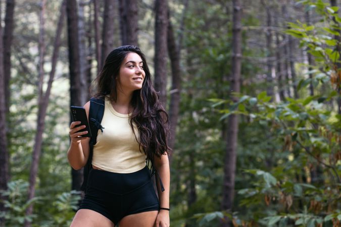 Young woman using her smartphone while hiking in the forest