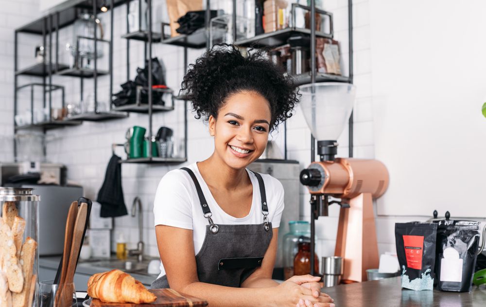 Happy barista leaning on the counter of cafe