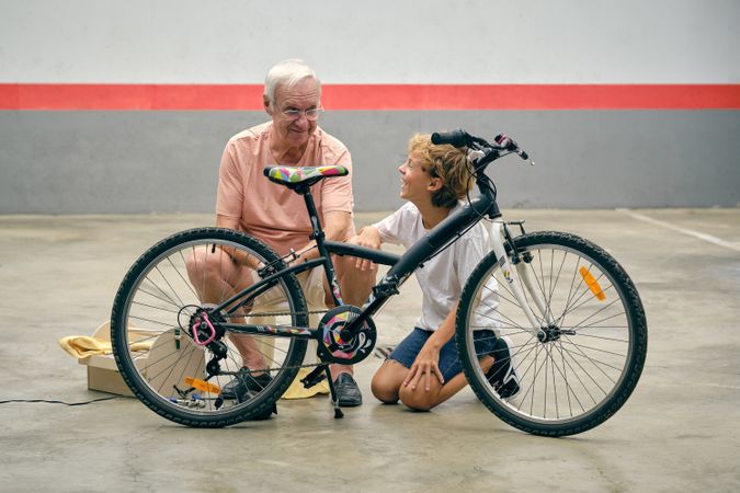Smiling grandfather talking to grandson while fixing bicycle