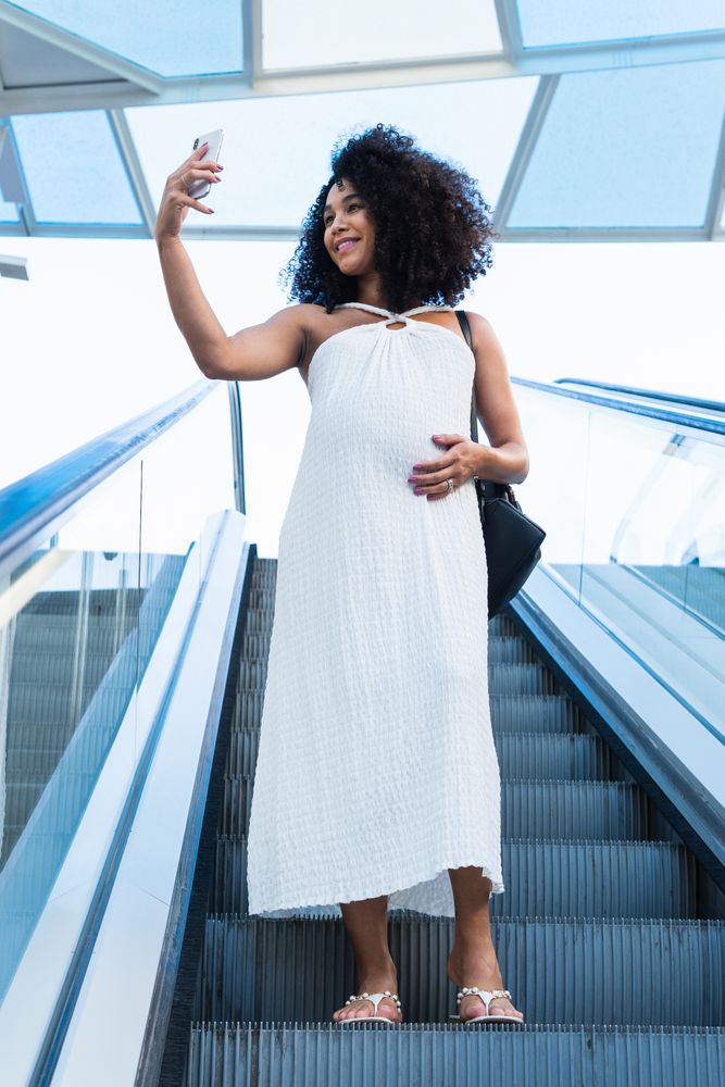 Pregnant Black woman taking self portrait on smartphone on escalator