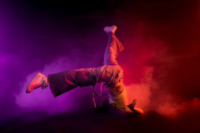 Young woman break dancing in colorful smoke