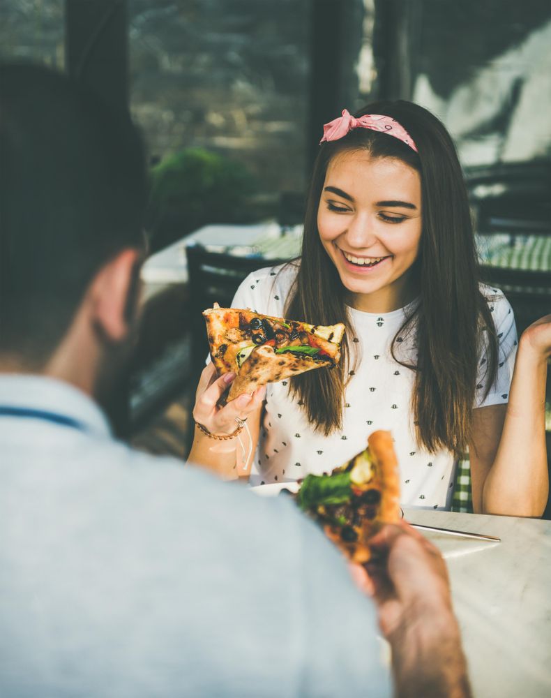 Couple eating pizza al fresco, woman smiling