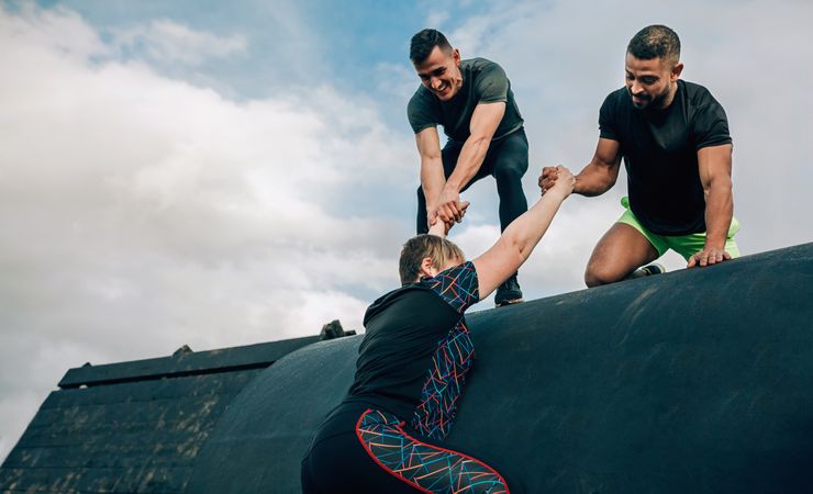 Woman in an obstacle course climbing a drum with teammates
