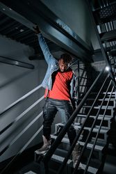 Black person putting on jeans jacket on staircase