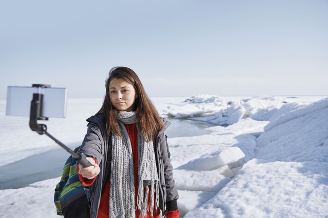 Female traveler outdoors at icy landscape using monopod to make