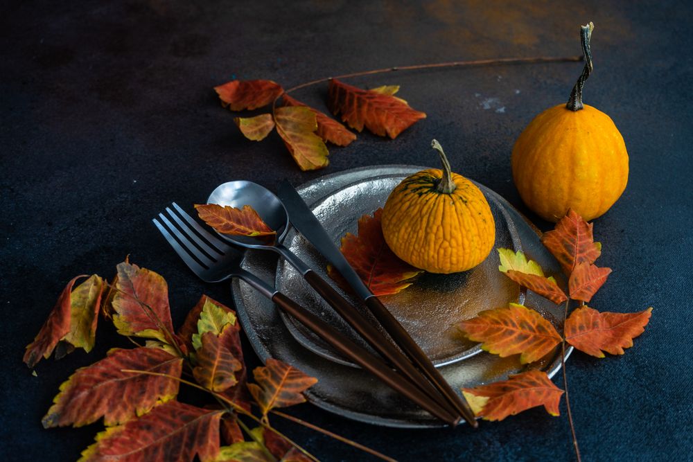 Table settings of shiny ceramic plates with autumn leaves and cutlery