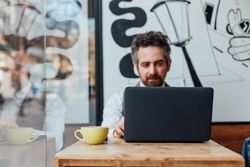 Man sits in window of cafe with laptop