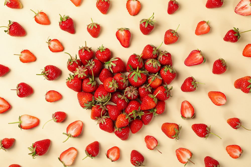Heart made of tasty strawberry on beige background, top view. Summer berry