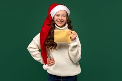 Smiling girl in Santa hat holding golden envelope.