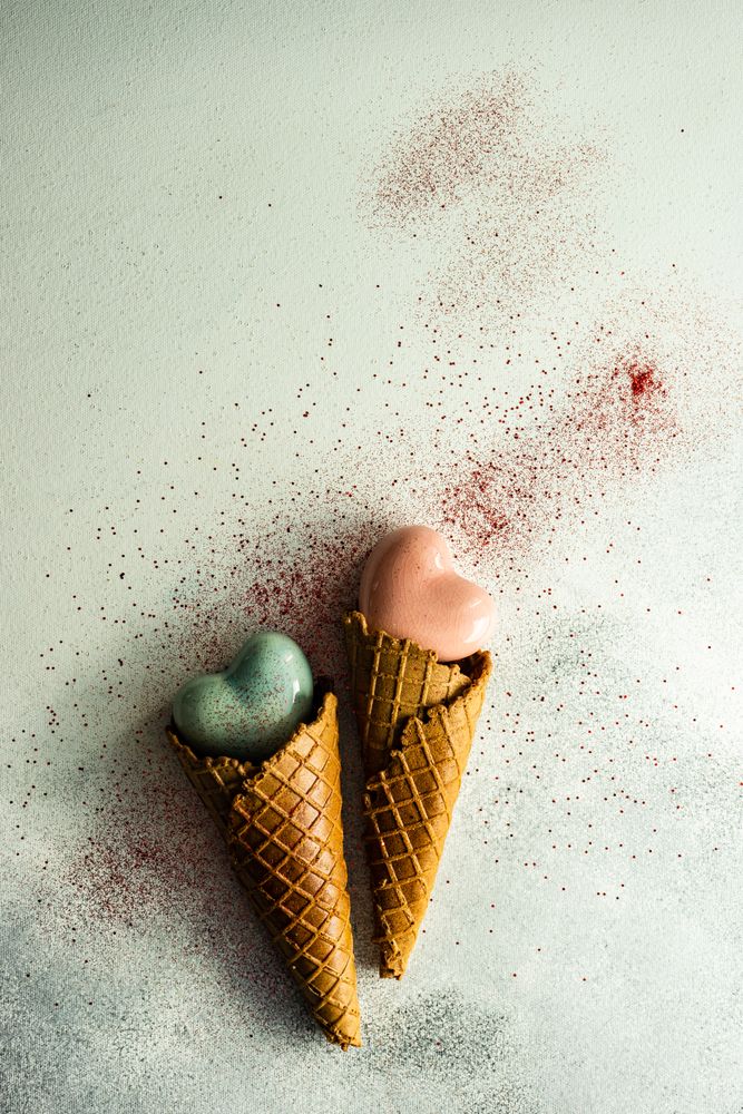 Two ceramic hearts in waffle cones on grey background with glitter
