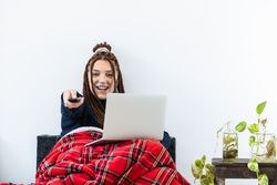 Woman with dreadlocks working with a laptop at home and with a remote control in hand
