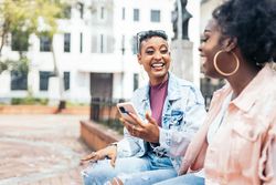 Black women friends using smartphone having fun in the city