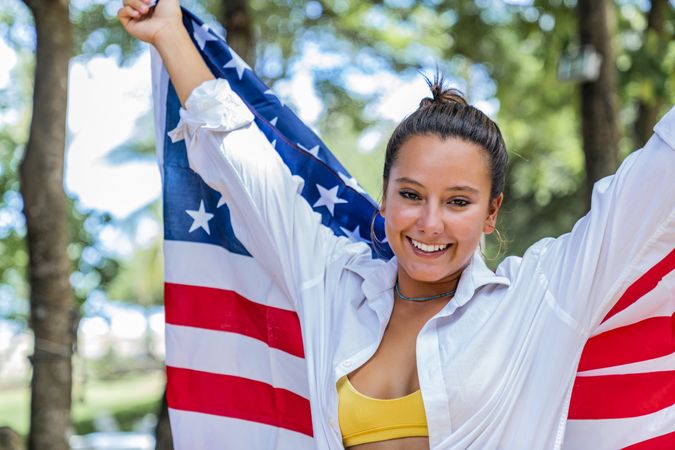 Content woman smiling wrapped in American flag walking along park