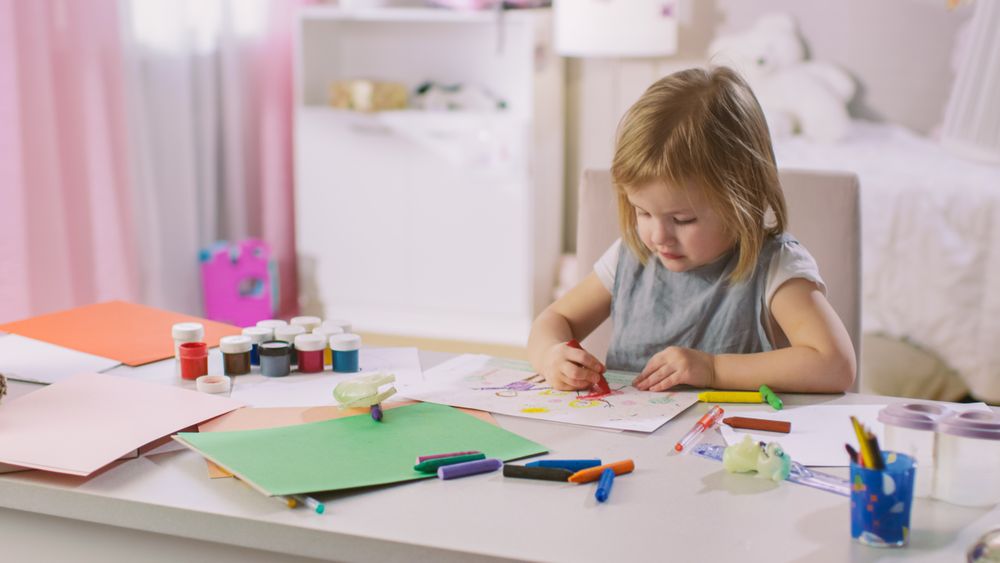 Cute Little Girl Sits at Her Table and Draws with Crayons.