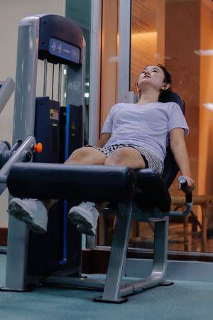 woman using leg extension machine at gym. sitting with legs positioned under padded machine bar.