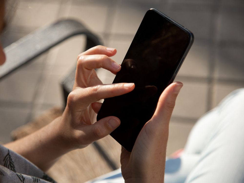 The hands of a young woman, using a smartphone sitting on a bench outside