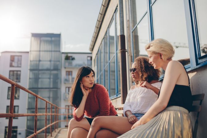 Three young women sitting outdoors and chatting on city patio