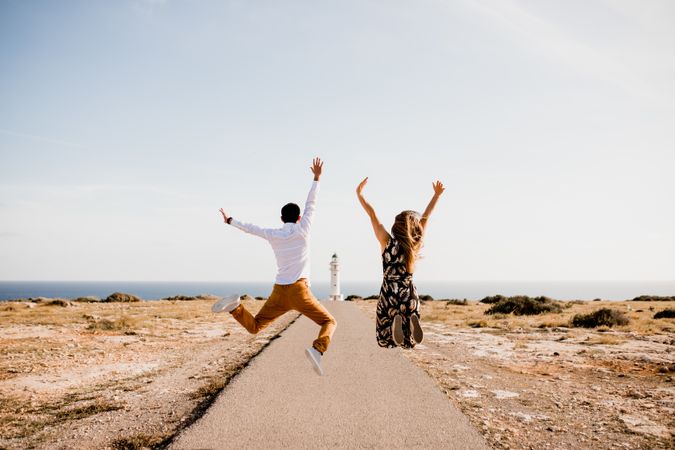 Joyful couple jumping with arms raised on way to seashore