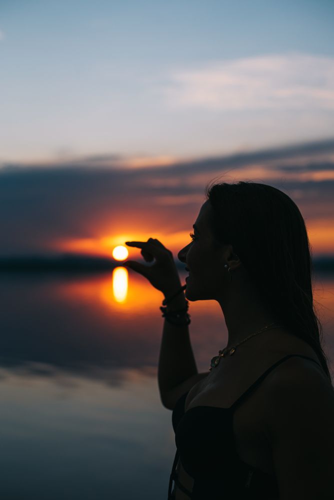 Content woman in swimwear holding sun on beach at sunset