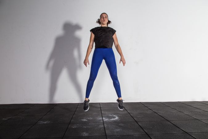 athletic young woman in sportswear doing squats and jumping in gym