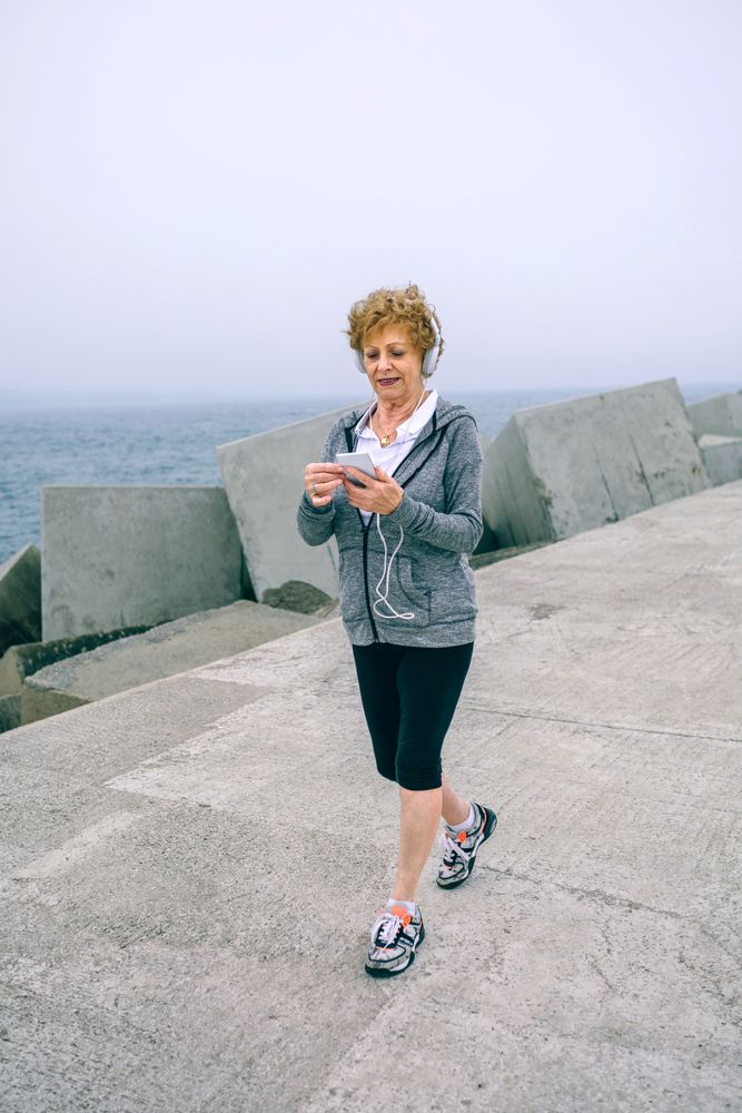 Mature sportswoman walking and looking at her smartphone