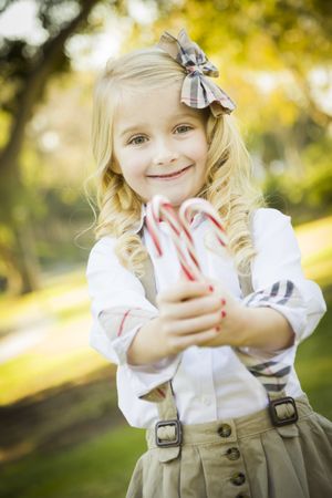 Cute Little Girl Holding Christmas Candy Canes Outdoors.