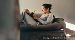Smiling woman talking to her baby sitting on a couch at home 0PGG2b